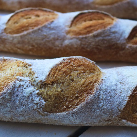 Close-up of a gluten-free baguette with a rustic crust on a wooden surface.