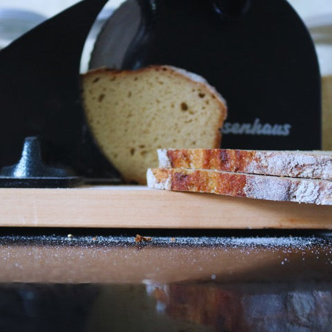 Sliced bread on a wooden cutting board with a black knife in the background.