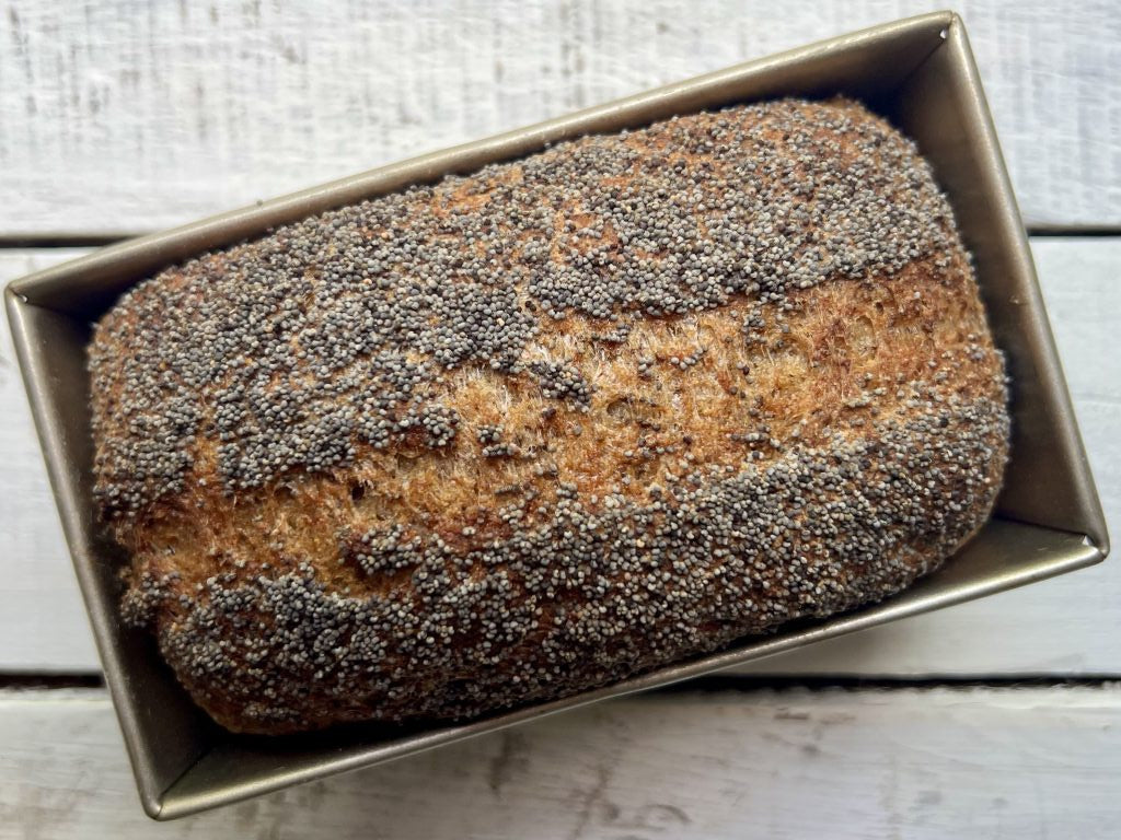 Loaf of bread with poppy seeds in a baking pan on a wooden surface