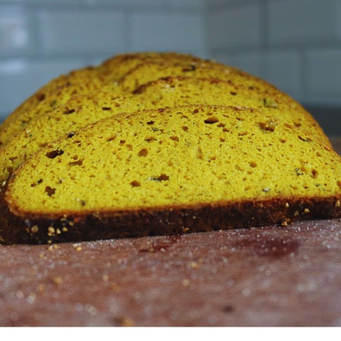 Loaf of gluten-free turmeric miso black pepper sourdough bread with a textured surface on a tiled wall background
